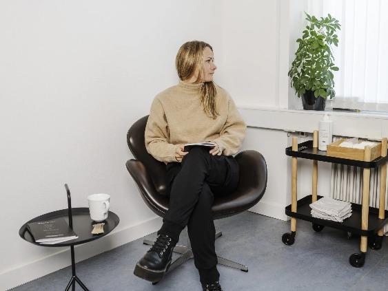 En kvinde sidder i en moderne stol i et lyst rum med en plante og et lille bord ved siden af.