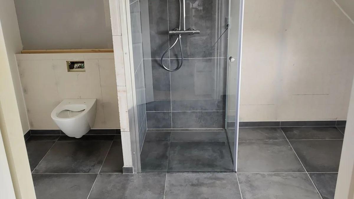 Moderne badeværelse med bruseniche, væghængt toilet og grå fliser på gulvet.