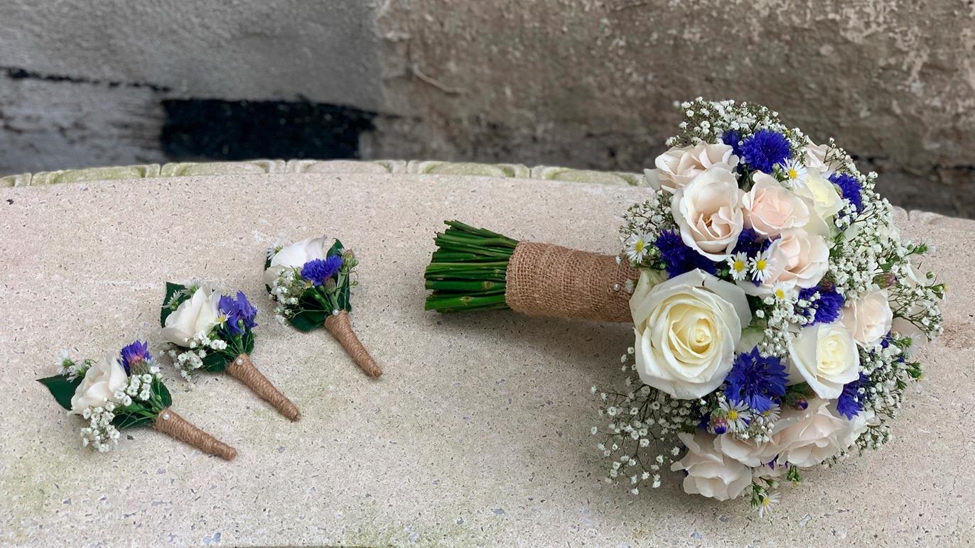 En smuk brudebuket med hvide roser og blå kornblomster, samt tre matchende boutonniere.