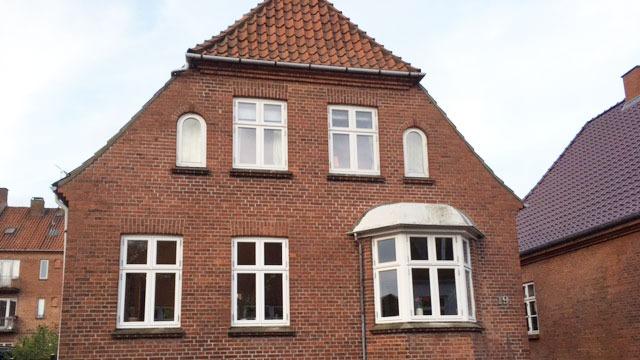 Rødt murstenshus med skråtag og flere vinduer i forskellige former.
