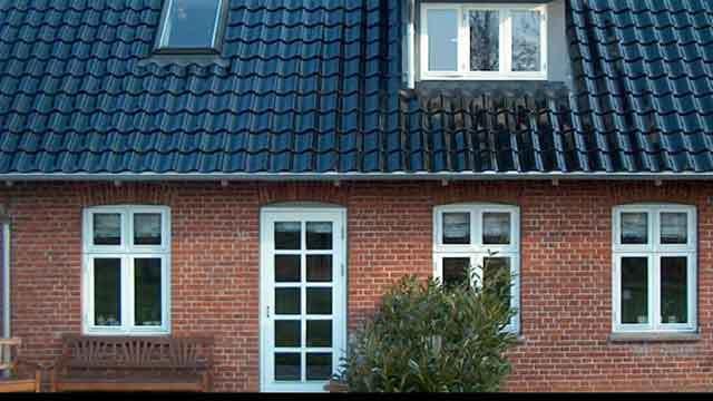 En rød murstenshus med sort tag og flere vinduer, beliggende i en rolig boligområde.