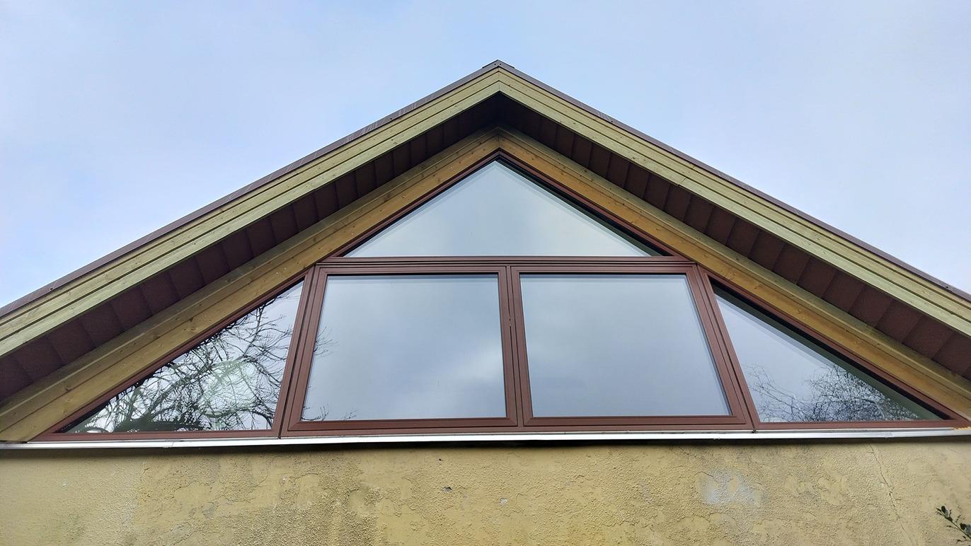 Et hus med en spids tagryg og store vinduer, der reflekterer himlen.
