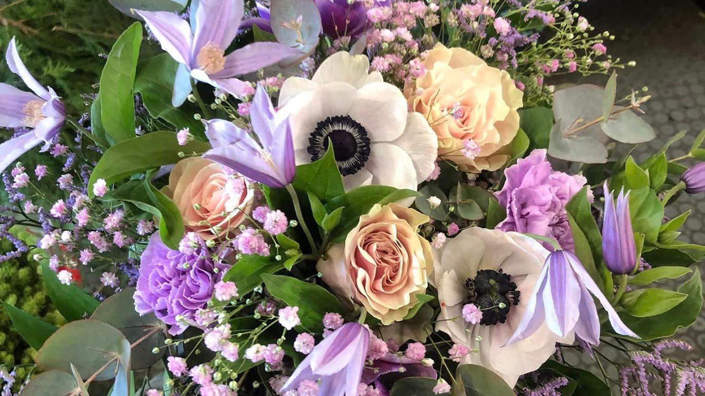 En smuk buket med lyserøde roser, anemoner og lilla blomster, omkranset af grønne blade.