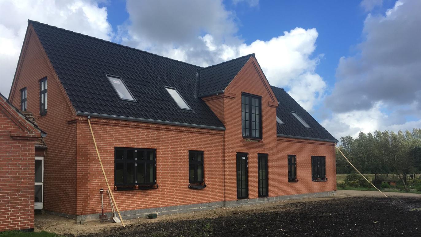 Et moderne murstenshus med sort tag og store vinduer under en blå himmel med skyer.