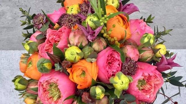 En farverig buket med lyserøde, orange og gule blomster samt grønne knopper.