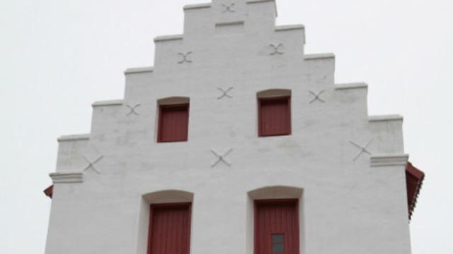Hvid bygning med rødmalede vinduer og en karakteristisk gavl med dekorative detaljer.