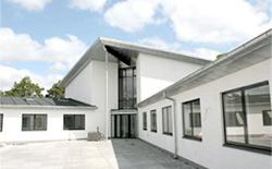 Moderne hvidt hus med store vinduer og en glasindgang under en blå himmel.