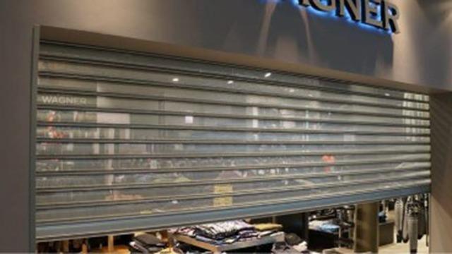 Lukket butik med rullejalousi foran vinduet og tøj synligt bag glasset.