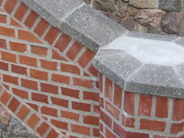 Murstensvæg med grå betonoverflade og detaljer i rød teglsten, der viser en dekorativ konstruktion.
