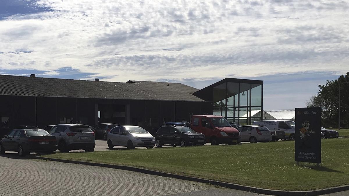 En bygning med glasfacade og parkerede biler på en græsplæne under en skyet himmel.