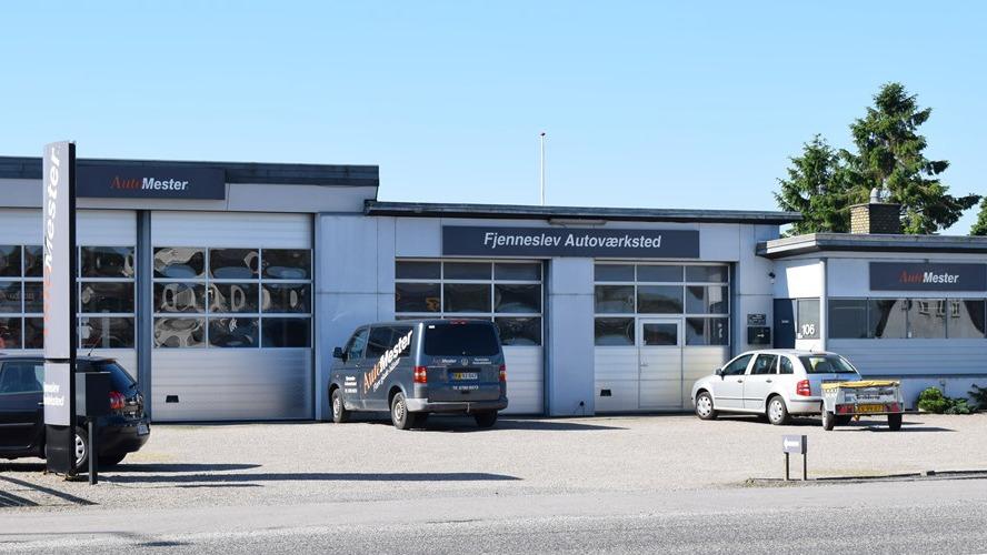 Bilforhandler med flere biler parkeret foran bygningen og en klar blå himmel i baggrunden.