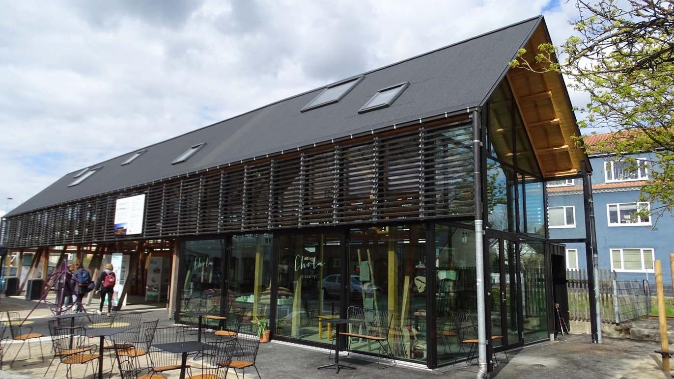 Moderne bygning med glasfacade og trædetaljer, omgivet af caféborde og stole.
