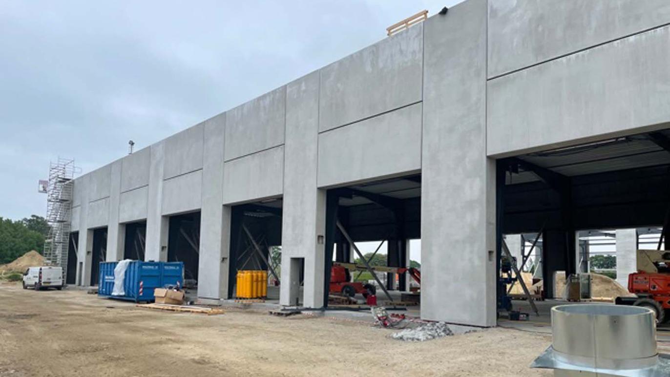 Bygning under konstruktion med grå betonvægge, åbne porte og byggeudstyr på en byggeplads.