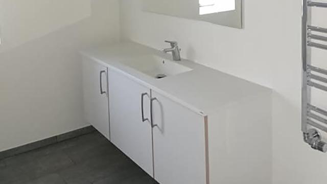 Moderne badeværelse med hvidt skab, håndvask og spejl på væggen. Fliser på gulvet.
