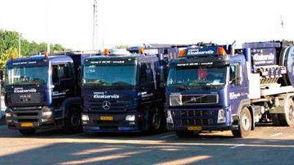 Tre lastbiler parkeret på en gårdsplads, alle med blå farve og logoer fra et transportfirma.