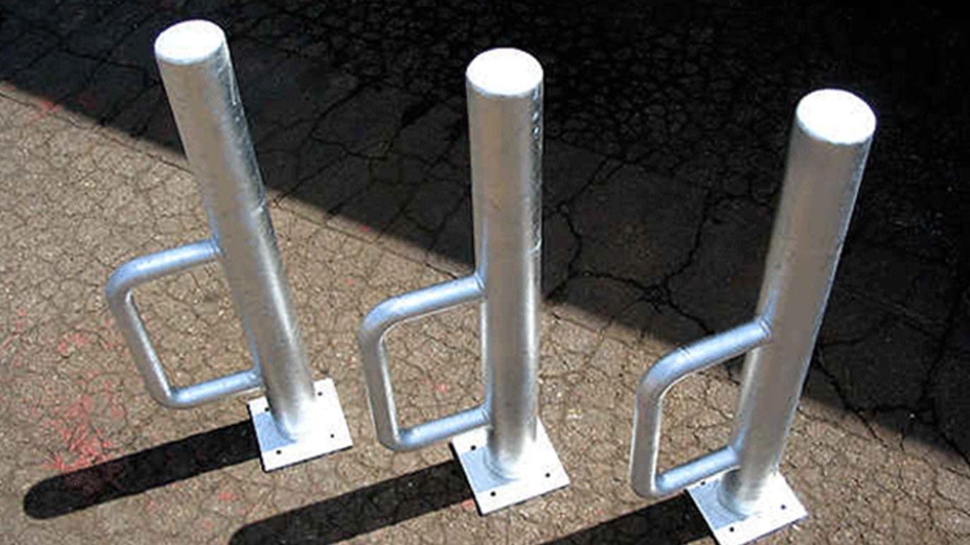 Tre metalstolper med håndtag, der står på en asfaltbelægning, skaber en barriere.