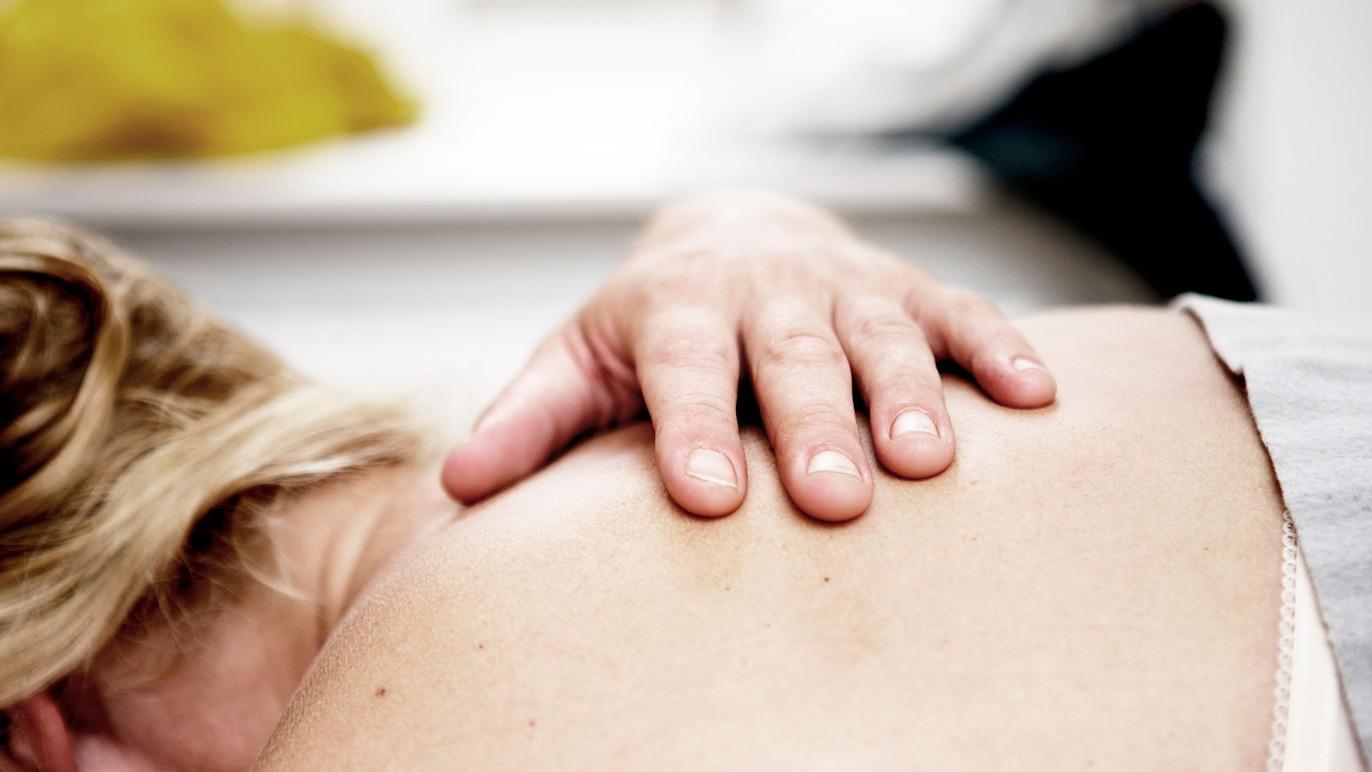 Hånd på en persons skulder under en afslappende massage i et lyst rum.