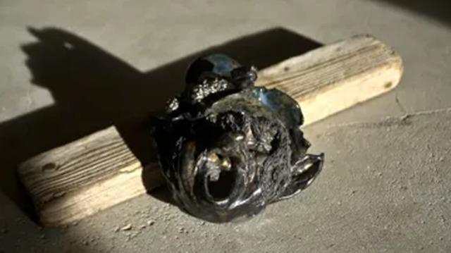 En sort skulptur af en ansigt med detaljer, placeret på en træplade på en betonoverflade.