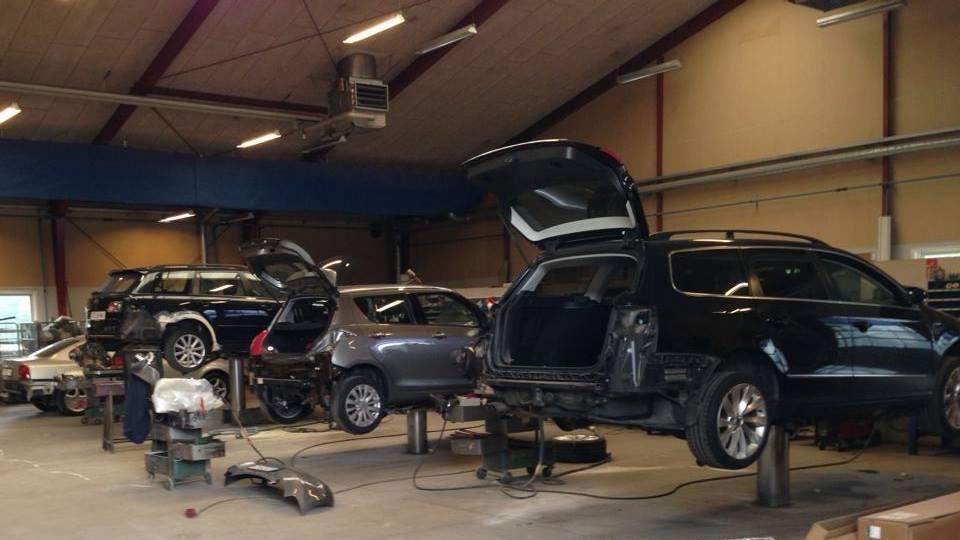 Et bilværksted med flere biler på lifte, hvor motorer og dele bliver repareret.