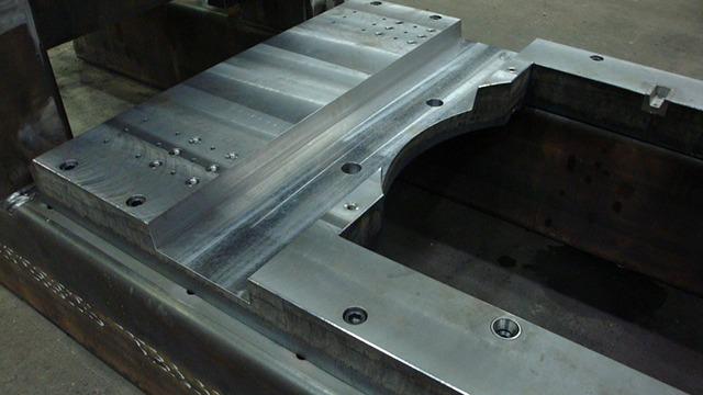 Detalje af en metalbearbejdet komponent med præcise udskæringer og skruer i en industriel værksted.