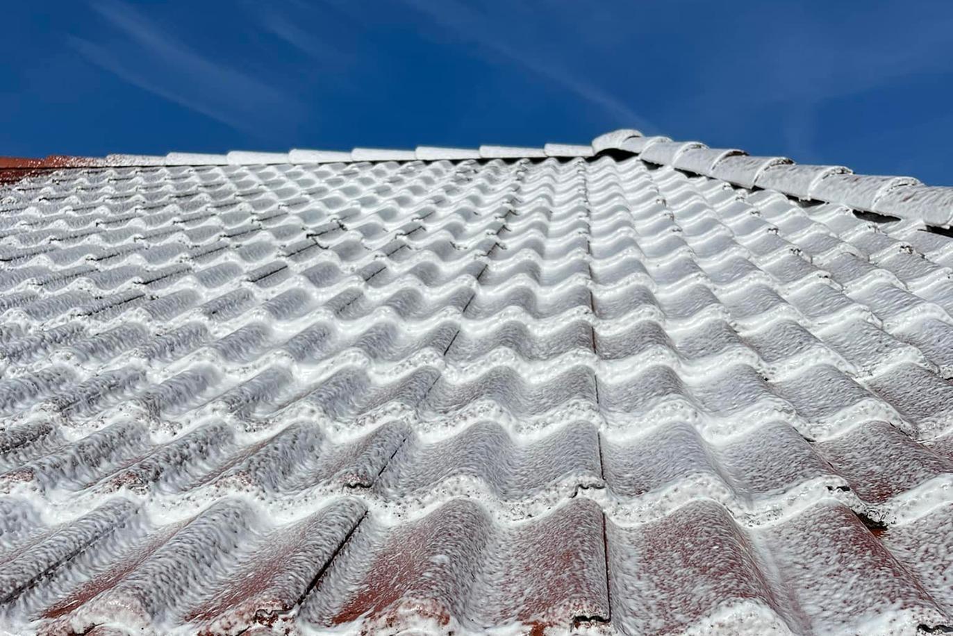 Taget af et tag dækket af sne med bølgede tagplader under en klar blå himmel.