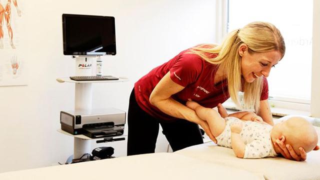 En fysioterapeut hjælper en baby med øvelser i et behandlingsrum med medicinsk udstyr.