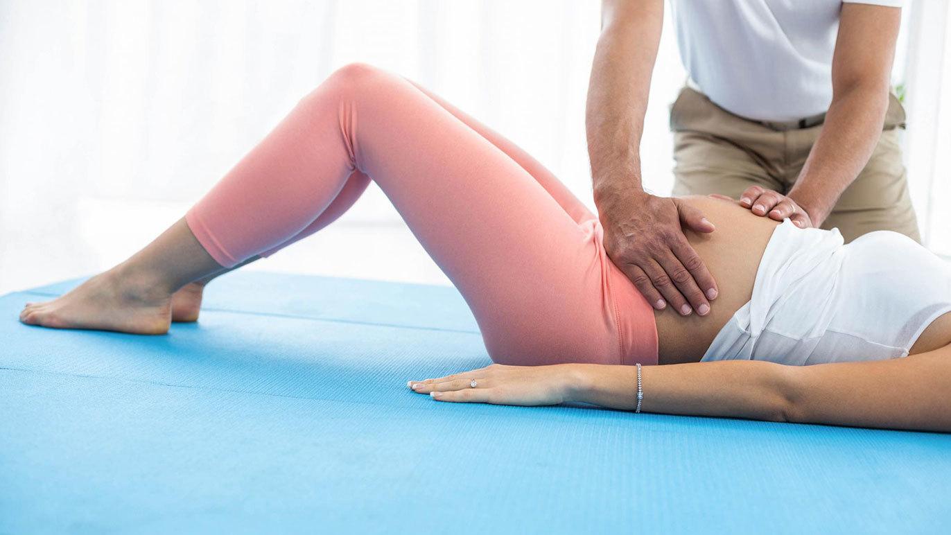 En gravid kvinde ligger på en træningsmåtte, mens en mand rører ved hendes mave for at give støtte.