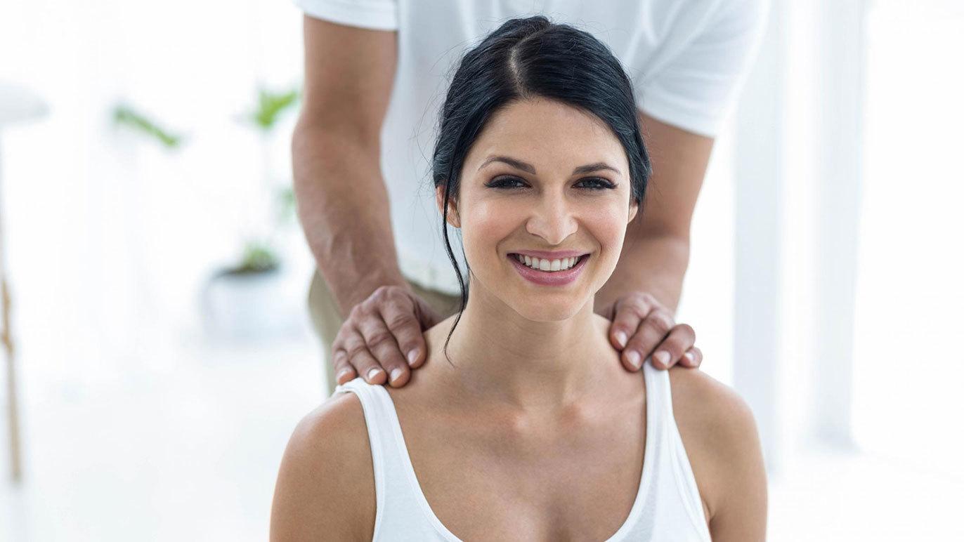En kvinde får massage af en mand i et lyst og moderne rum, mens hun smiler afslappet.