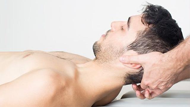Mand får nakkemassage på en behandlingsbriks med en behandler, der holder om hans hoved.
