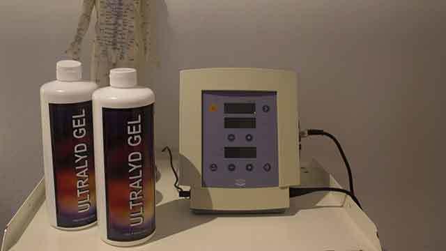 Ultralydsapparat med to flasker ultralydsgel på en hvid overflade.