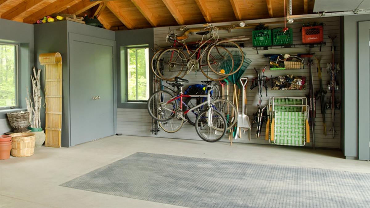 Et garageinteriør med cykler, værktøj og opbevaringskasser på væggene samt en tom gulvplads.