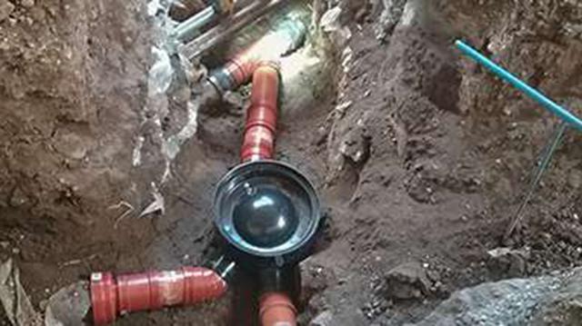 Gravested med rørinstallationer og en sort brønd i en dyb grøft, omgivet af jord og værktøj.