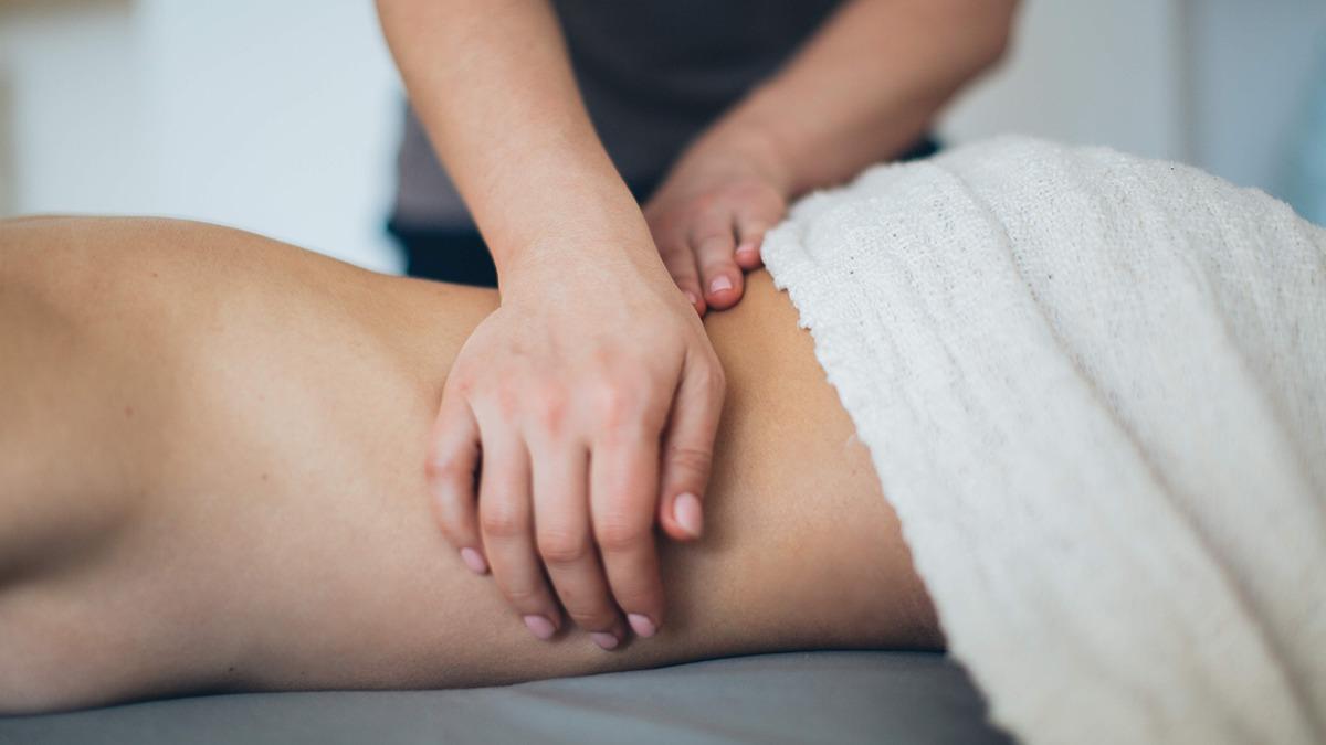 En person får massage på låret, mens en hånd trykker blidt på huden under et håndklæde.
