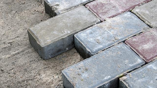 Nærbillede af stenbelægning med grå og røde sten, der ligger på en sandbund.
