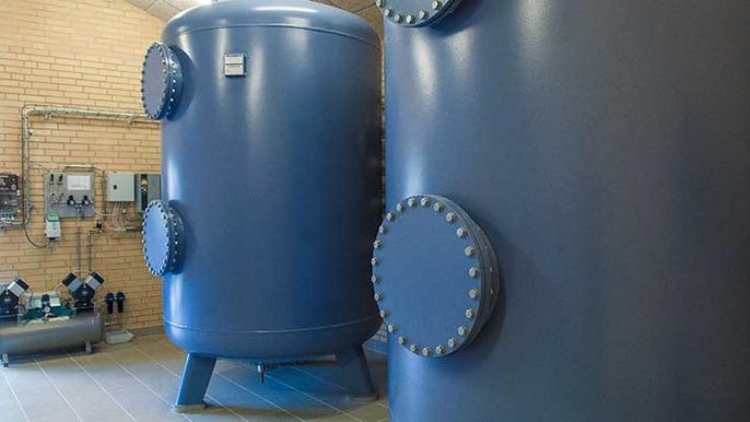 To store trykluft i store blå tryktanke i et industrielt rum med elektrisk udstyr.