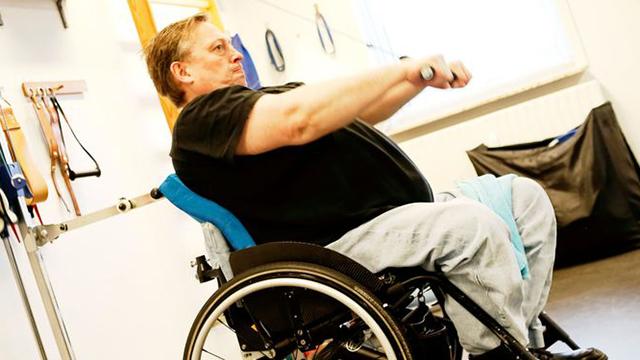 Mand i kørestol, der træner med håndtag i et fitnessrum.