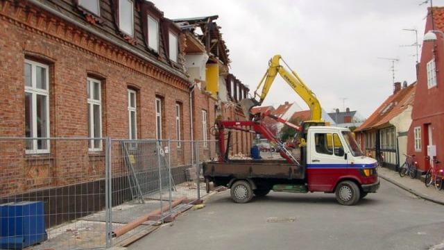 Byggeri med en kran og en lastbil ved en bygning under renovering i en gade med afspærring.