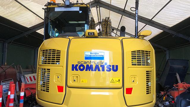 Gul Komatsu maskine parkeret i en hal med værktøj og udstyr i baggrunden.