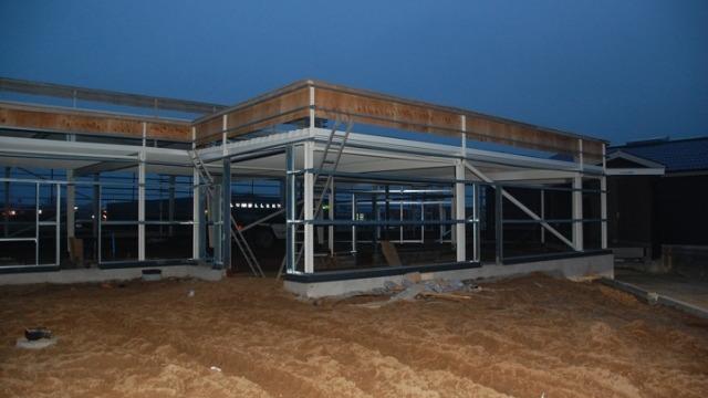 Byggeri af moderne bygning med stålramme og glasvægge, beliggende på en sandet grund ved skumring.
