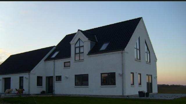 Moderne hvidt hus med skråtag og store vinduer i solnedgang. Græsplæne foran huset.