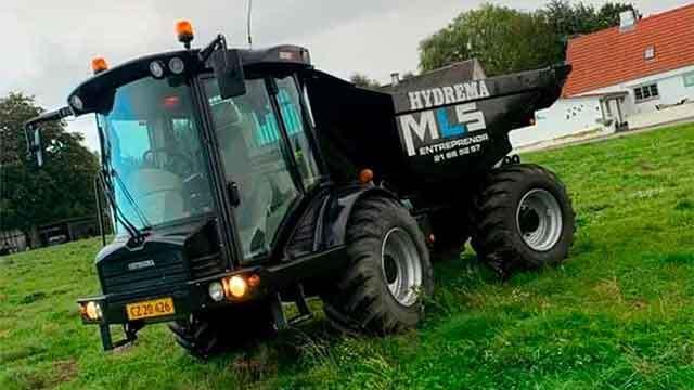 En sort Hydrema M5 dumpertraktor parkeret på en grøn mark med en hvid bygning i baggrunden.