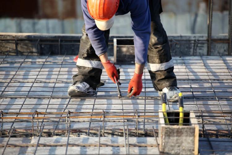 En arbejder i orange hjelm og handsker, der arbejder med armeringsjern på en byggeplads.