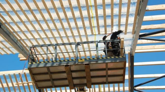 En håndværker arbejder på en stillads under en byggekonstruktion med træbjælker.