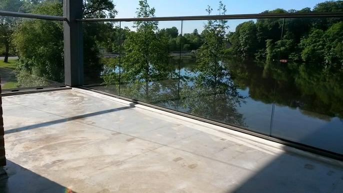 Udsigt fra en balkon med glasrækværk over en sø omgivet af grønne træer.