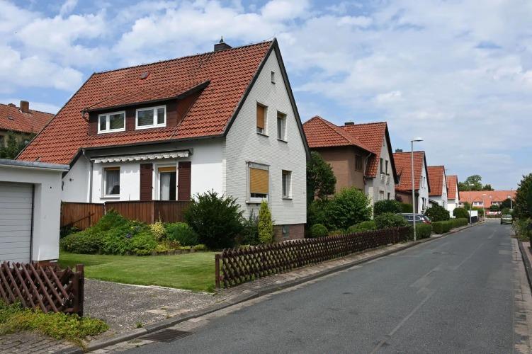 En stille gade med huse med røde tage, grønne haver og en klar blå himmel i baggrunden.