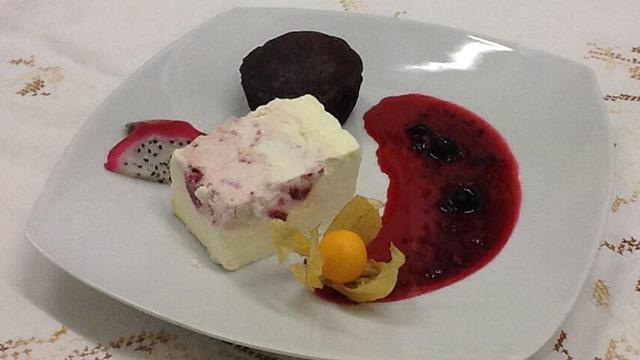 En desserttallerken med chokoladefondant, islagkage og bærkompot, pyntet med en physalis.