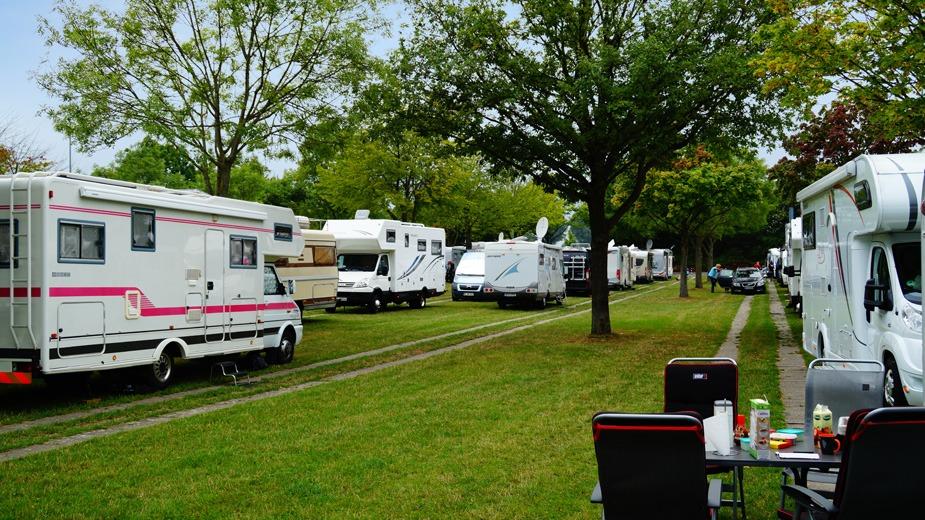 Campingplads med flere campingvogne parkeret langs en græsplæne under træer.