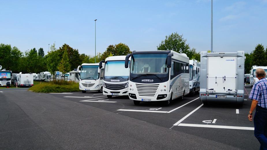 En campingplads med flere autocampere parkeret i rækker under en blå himmel.