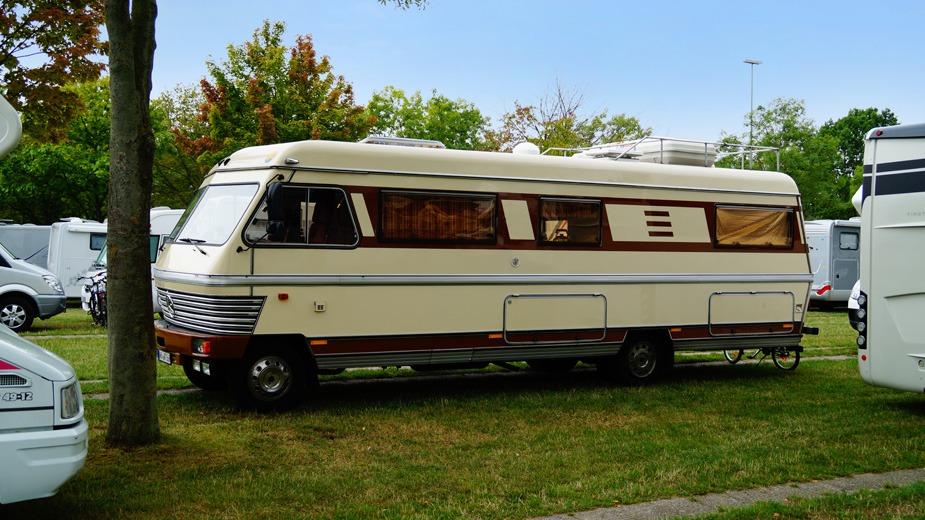 En vintage campingvogn parkeret på græsset blandt træer og andre campingvogne.