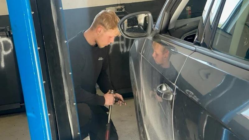 En mekaniker arbejder på en bil i et værksted med værktøj i hånden.